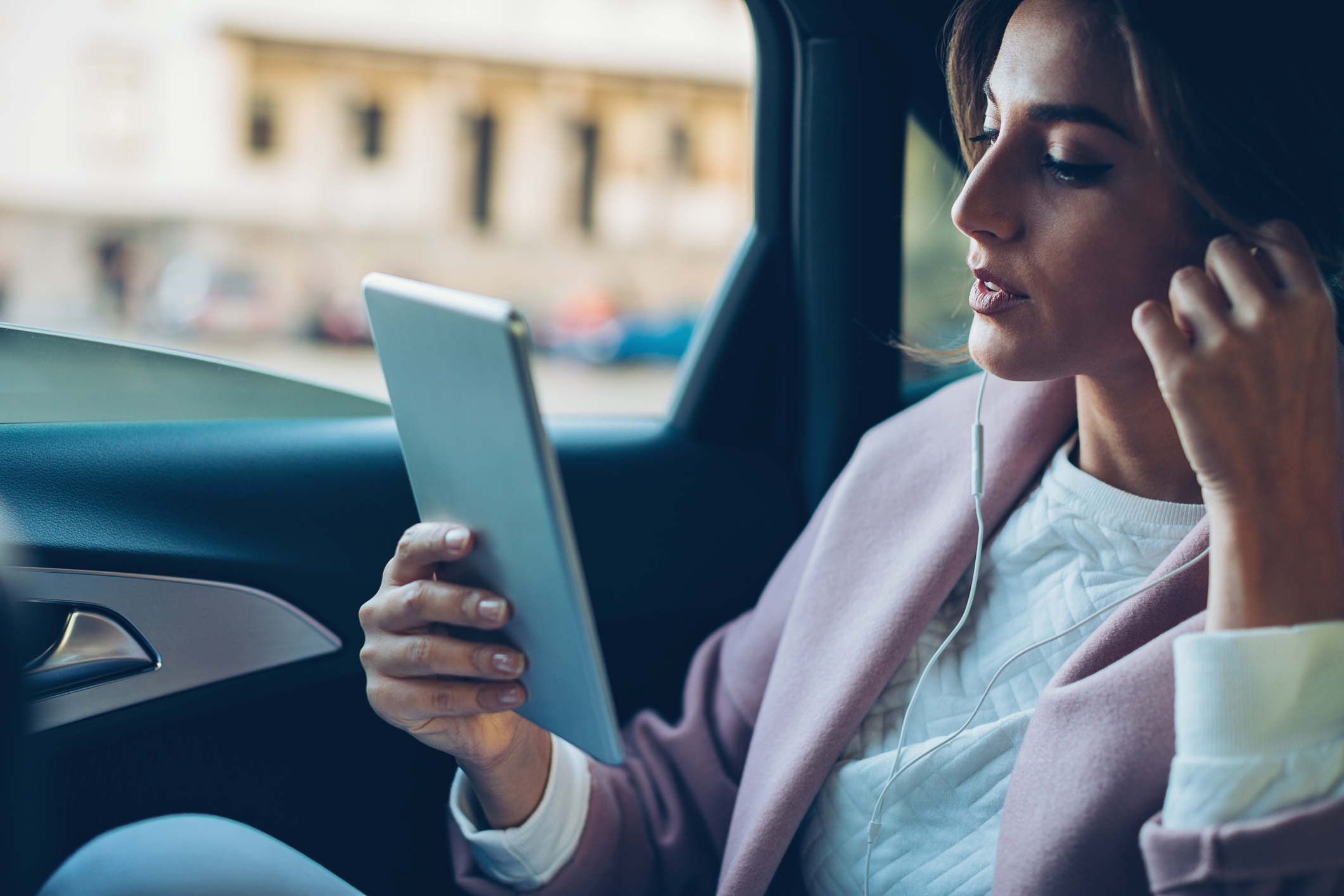 Beautiful woman using digital tablet on the back seat of a car